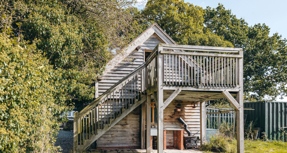 Wooden shed with stairs and balcony, surrounded by trees.