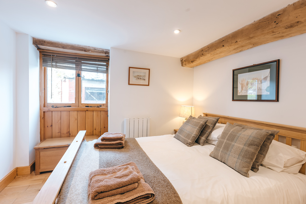 Bedroom with bed, wooden beams, and small window.