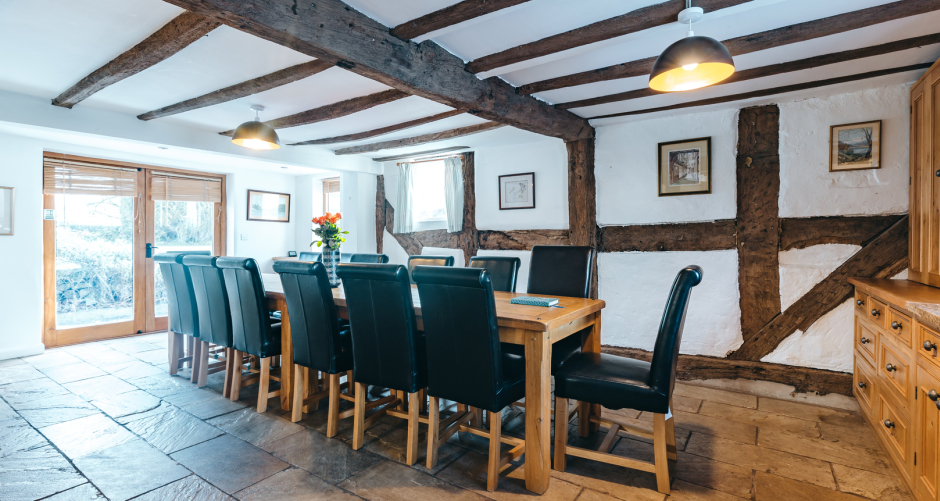 Dining room with long table, wooden beams, chairs.
